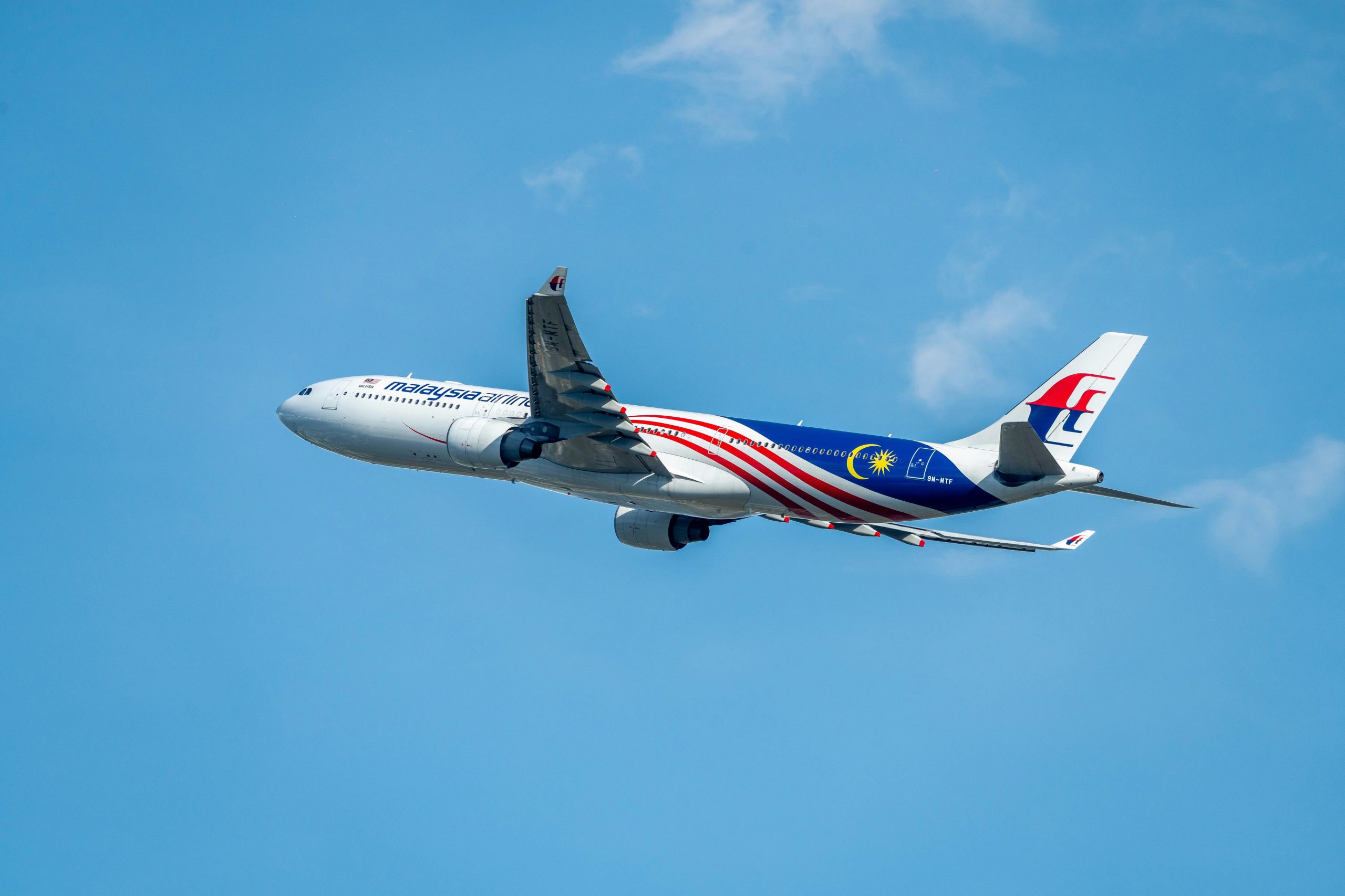 A Malaysia Airlines aircraft flying against a clear blue sky, showcasing its design.